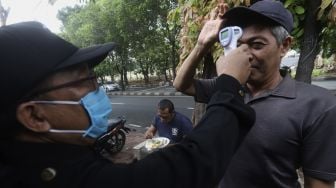 Petugas memeriksa suhu tubuh seorang warga sebelum menyantap hidangan makan gratis di Jalan Jenderal Basuki Rachmat, Cipinang Besar Selatan, Jakarta, Rabu (5/8/2020). [Suara.com/Angga Budhiyanto]