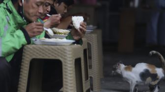 Sejumlah warga menyantap hidangan makan gratis di Jalan Jenderal Basuki Rachmat, Cipinang Besar Selatan, Jakarta, Rabu (5/8/2020). [Suara.com/Angga Budhiyanto]