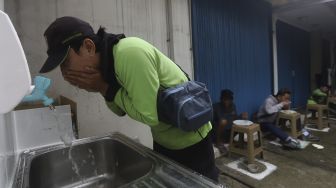 Seorang warga mencuci tangan sebelum menyantap hidangan makan gratis di Jalan Jenderal Basuki Rachmat, Cipinang Besar Selatan, Jakarta, Rabu (5/8/2020). [Suara.com/Angga Budhiyanto]