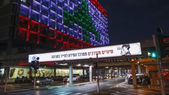 Pesepeda melintas di depan Gedung Balai Kota yang diterangi dengan bendera Lebanon di Tel Aviv, Israel, Rabu (5/8). [Jack Guez/AFP]
