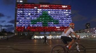 Pesepeda melintas di depan Gedung Balai Kota yang diterangi dengan bendera Lebanon di Tel Aviv, Israel, Rabu (5/8). [Jack Guez/AFP]
