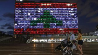 Pesepeda melintas di depan Gedung Balai Kota yang diterangi dengan bendera Lebanon di Tel Aviv, Israel, Rabu (5/8). [Jack Guez/AFP]
