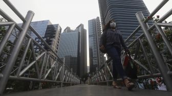 Pekerja melintas di waktu pulang kerja di jembatan penyeberangan orang (JPO) tanpa atap di kawasan Sudirman, Jakarta, Kamis (6/8/2020). [Suara.com/Angga Budhiyanto]