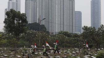 Petugas Pertamanan dan Kehutanan Kota Jakarta Pusat berjalan mengenakan atribut kemerdekaan usai memangkas rumput di TPU Karet Bivak, Tanah Abang, Jakarta Pusat, Minggu (16/8/2020). [Suara.com/Angga Budhiyanto]