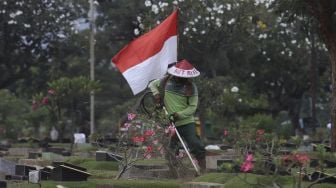 Seorang petugas Pertamanan dan Kehutanan Kota Jakarta Pusat mengenakan atribut kemerdekaan saat memangkas rumput di TPU Karet Bivak, Tanah Abang, Jakarta Pusat, Minggu (16/8/2020). [Suara.com/Angga Budhiyanto]