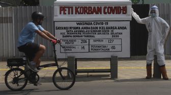 Pesepeda melintas di depan seni instalasi tenaga medis yang sedang memegang peti jenazah korban COVID-19 di simpang jalan Kemang 1, Jakarta Selatan, Minggu (16/8/2020). [Suara.com/Angga Budhiyanto]