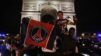 Suporter Paris Saint-Germain (PSG) membentangkan bendera PSG saat merayakan kemenangan 3-0 tim mereka atas RB Leipzig yang membuat PSG lolos ke final Liga Champions di Champs-Elysees Avenue dekat Arc de Triomphe, Paris, Perancis, Rabu (19/8) dini hari WIB.  [GEOFFROY VAN DER HASSELT / AFP]