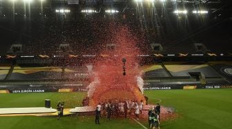 Para pemain Sevilla merayakan dengan trofi setelah memenangkan pertandingan final sepak bola UEFA Europa League Sevilla melawan Inter Milan di RheinEnergieStadion, Cologne, Jerman pada (21/8/2020). [Ina Fassbender / POOL / AFP]