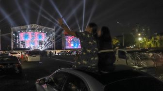 Dua orang penonton berswafoto dari atap mobilnya saat gelaran konser drive-in di Jiexpo Kemayoran, Jakarta Pusat, Minggu (30/8). [Suara.com/Alfian Winanto]