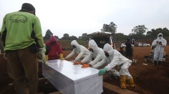 Petugas pemakaman penanganan jenazah pasien COVID-19 menurunkan peti jenazah ke dalam pusara di TPU Pondok Ranggon, Jakarta, Rabu (2/9/2020). [Suara.com/Angga Budhiyanto]