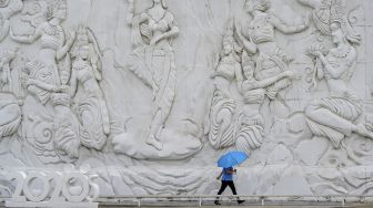 Seorang karyawan memegang payung sambil berjalan di depan dinding yang terbuat dari pasir putih menyerupai es di taman "Frost Magical Ice of Siam" di luar Pattaya, Thailand (2/9/2020). [Mladen ANTONOV / AFP]