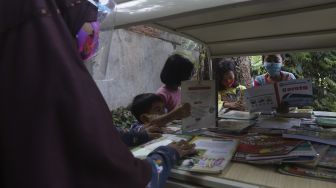 Sejumlah anak membaca buku koleksi dari Bemo Baca milik Sutino (60) bertepatan dengan Hari Aksara Internasional (HAI) di Jakarta, Selasa (8/9/2020). [Suara.com/Angga Budhiyanto]