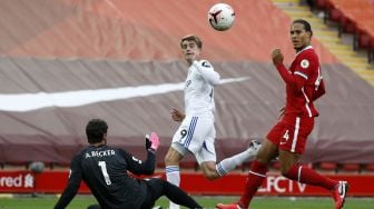 Striker Leeds United Patrick Bamford (tengah) menendang bola ke atas kiper Liverpool Alisson Becker (kiri) untuk mencetak gol kedua mereka  selama pertandingan sepak bola Liga Premier Inggris antara Liverpool melawan Leeds United di Anfield, Liverpool, Inggris, Mingggu (13/9) dini hari WIB. [PHIL NOBLE / POOL / AFP]
