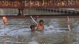 Anak - anak bermain air saat berenang di saluran Kalimalang, Kalimalang, Jakarta Timur, Selasa (15/9). [Suara.com/Alfian Winanto]