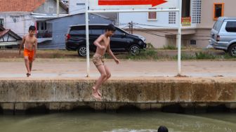 Anak - anak melompat ke dalam air saat berenang di saluran Kalimalang, Kalimalang, Jakarta Timur, Selasa (15/9). [Suara.com/Alfian Winanto]