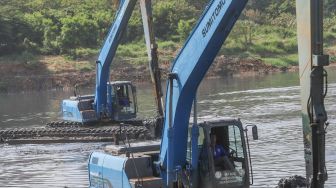 Dua orang petugas mengoperasikan alat berat untuk mengeruk lumpur di Waduk Ria Rio, Pulo Gadung, Jakarta Timur, Selasa (22/9). [Suara.com/Alfian Winanto]