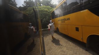 Petugas memakai alat pelindung diri menyemprotkan cairan disinfektan pada bagian luar bus sekolah di Posko Gabungan PSBB dan Gakplin Protkes, Kramat Jati, Jakarta, Kamis (24/9/2020). [Suara.com/Angga Budhiyanto]