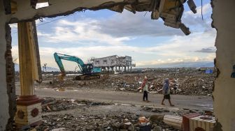 Warga melintas di depan puing rumah yang hancur akibat tsunami dan belum dirobohkan di Palu, Sulawesi tengah, Minggu (27/9/2020). [ANTARAFOTO/Basri Marzuki]
