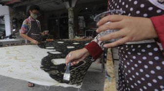 Restu Rizky Ramadhan (13) dibantu Ibunya menyelesaikan proses pembuatan motif batik di Rumah Batik Palbatu, Jakarta, Jumat (2/10/2020). [Suara.com/Angga Budhiyanto]