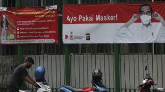 Seorang pengendara motor memarkirkan motornya di depan spanduk imbauan menggunakan masker di kawasan MH Thamrin, Jakarta, Jumat (2/10/2020). [Suara.com/Angga Budiyanto]