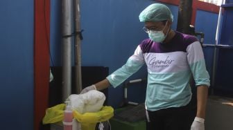 Petugas medis memasukkan baju hazmat ke tempat pembuangan khusus sampah medis sebelum membersihkan diri (dekontaminasi) usia bertugas menangani pasien COVID-19 di Puskesmas Kecamatan Gambir, Jakarta, Selasa (6/10/2020). [Suara.com/Angga Budhiyanto]