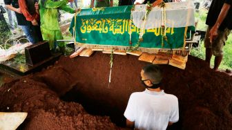 Musisi Rayi Putra Rahardjo atau Rayi RAN masuk ke liang lahad membantu proses pemakaman sang Ibu di TPU Karet Bivak, Jakarta Pusat, Jumat (9/10). [Suara.com/Alfian Winanto]