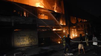 Petugas Pemadam Kebakaran dibantu warga memadamkan api yang menghanguskan bangunan bioskop Grand Theater di kawasan Senen, Jakarta, Kamis (8/10/2020) malam.  [ANTARA FOTO/Indrianto Eko Suwarso]