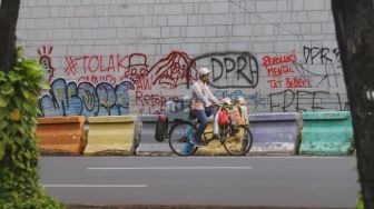 Pedagang kopi keliling melintas didepan dinding Kedutaan Besar Amerika Serikat yang masih dipenuhi coretan aksi demo tolak Omnibus Law Kamis (8/10) lalu di Jalan Merdeka Selatan, Jakarta Pusat, Sabtu (10/10). [Suara.com/Alfian Winanto]