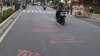 Warga melintas dijalan yang masih dipenuhi coretan aksi demo tolak Omnibus Law Kamis (8/10) lalu di Jalan Cikini Raya, Jakarta Pusat, Sabtu (10/10). [Suara.com/Alfian Winanto]