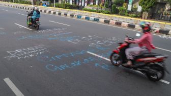 Warga melintas dijalan Ridwan Rais yang masih dipenuhi coretan aksi demo tolak Omnibus Law Kamis lalu di Jakarta Pusat, Sabtu (10/10). [Suara.com/Alfian Winanto]