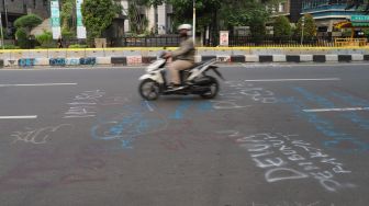 Warga melintas dijalan Ridwan Rais yang masih dipenuhi coretan aksi demo tolak Omnibus Law Kamis lalu di Jakarta Pusat, Sabtu (10/10). [Suara.com/Alfian Winanto]