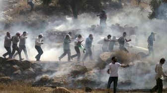 Pengunjuk rasa Palestina berlarian di tengah asap gas air mata selama bentrokan dengan pasukan keamanan Israel di dekat desa Beit Dajan, Palestina, pada (9/10/2020). [JAAFAR ASHTIYEH / AFP]