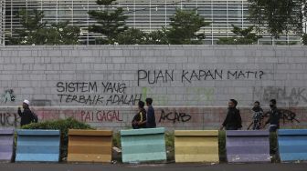 Sejumlah massa melintas di depan coretan berisi kritik kepada Dewan Perwakilan Rakyat di Kedutaan Besar Amerika Serikat, Jakarta, Selasa (13/10/2020). [Suara.com/Angga Budhiyanto]