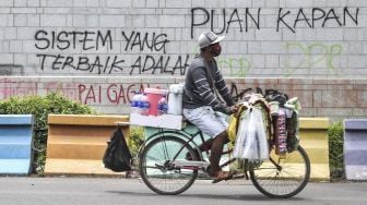 Penjual minuman mengayuh sepedanya di depan tembok yang dicoret-coret oleh orang tidak bertanggungjawab saat aksi Tolak UU Cipta Kerja di depan Kedutaan Amerika Serikat, Jakarta, Rabu (14/10/2020). [ANTARA FOTO/Muhammad Adimaja]