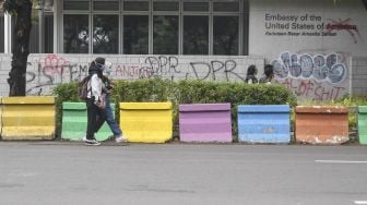 Warga berjalan di depan tembok yang dicoret-coret oleh orang tidak bertanggungjawab saat aksi Tolak UU Cipta Kerja di depan Kedutaan Besar Amerika Serikat, Jakarta, Rabu (14/10/2020).  [ANTARA FOTO/Muhammad Adimaja]