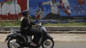 Pengendara motor melintas di depan mural tentang pandemi COVID-19 di Bukit Duri, Jakarta, Selasa (20/10/2020). [Suara.com/Angga Budhiyanto]