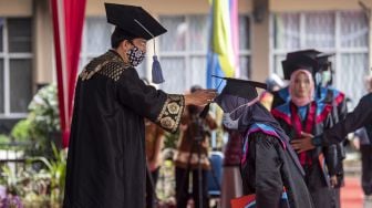 Direktur Politeknik Negeri Sriwijaya (Polsri) Ahmad Taqwa (kiri) memindahkan tali di topi toga wisudawan saat prosesi wisuda secara "Drive Thru" di Kampus Politeknik Negeri Sriwijaya (Polsri) Palembang, Sumatera Selatan, Sabtu (24/10/2020). [ANTARA FOTO/Nova Wahyudi]