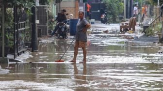 Seorang warga membersihkan lumpur sisa banjir di Perumahan Villa Jatirasa, Kota Bekasi, Jawa Barat, Minggu (25/10). [Suara.com/Alfian Winanto]