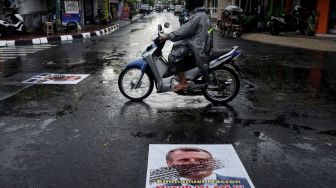 Pengendara melintas di atas poster berwajah presiden Prancis Emmanuel Macron yang ditempel di simpang Jalan Kauman, Yogyakarta, Rabu (28/10/2020).  [ANTARA FOTO/Andreas Fitri Atmoko]