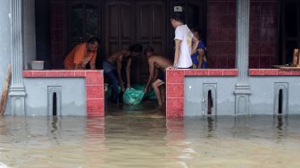 Warga menutup celah pintu rumahnya dengan karung berisi pasir saat banjir merendam kawasan jalan raya Gempol, Pasuruan, Jawa Timur, Senin (2/11/2020). [ANTARA FOTO/Umarul Faruq]