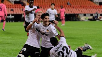 Gelandang  Valencia Carlos Soler (tengah) merayakan golnya bersama rekan satu timnya setelah mencetak gol ke gawang Real Madrid selama pertandingan sepak bola Liga Spanyol antara Valencia melawan Real Madrid di Stadion Mestalla, Valencia, Spanyol, Senin (9/11) dini hari WIB.  [JOSE JORDAN / AFP]