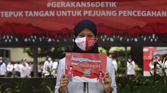 Seorang karyawan Kementerian Kesehatan membawa poster berisi seruan untuk menjaga kesehatan sebelum melakukan tepuk tangan secara bersama di depan Gedung Kementerian Kesehatan Republik Indonesia, Jakarta, Kamis (12/11/2020). [Suara.com/Angga Budhiyanto]