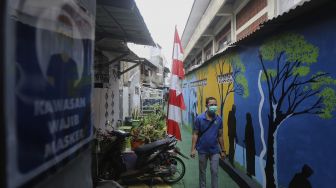 Warga melintas di salah satu gang yang dipenuhi mural di Kampung Sehat, Utan Kayu Selatan, Jakarta, Kamis (12/11/2020). [Suara.com/Angga Budhiyanto]