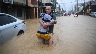 Warga megendong anaknya saat menerobos banjir akibat Topan Vamco,  di Manila, Filipina, Kamis (12/11/2020).  [Ted ALJIBE / AFP]