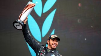 Pebalap Mercedes Lewis Hamilton mengangkat trofi di podium usai memenangi balapan F1 Grand Prix Turki di Istanbul, Minggu (15/11/2020). Pebalap kebanggaan Mercedes, Lewis Hamilton menjuarai F1 GP Turki, sekaligus menyegel gelar juara dunia ketujuhnya. [TOLGA BOZOGLU / POOL / AFP]

