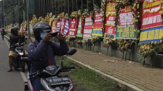 Pengendara sepeda motor berhenti untuk mengabadikan karangan bunga berisi dukungan terhadap TNI dalam upaya penegakan protokol kesehatan di depan Markas Kodam Jaya, Kramat Jati, Jakarta, Senin (23/11/2020). [Suara.com/Angga Budhiyanto]