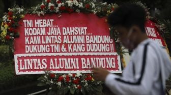 Warga berdiri di depan karangan bunga berisi dukungan terhadap TNI dalam upaya penegakan protokol kesehatan di depan Markas Kodam Jaya, Kramat Jati, Jakarta, Senin (23/11/2020). [Suara.com/Angga Budhiyanto]