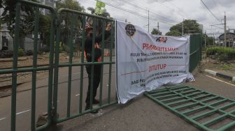 Petugas memasang spanduk penutupan perlintasan sebidang di kawasan Stasiun Palmerah, Jakarta, Minggu (29/11/2020). [Suara.com/Angga Budhiyanto]