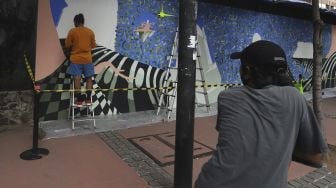 Pesepeda berhenti untuk melihat proses pembuatan seni mural berisi "Kampanye Bersihkan Udara di Banyak Kota di Seluruh Dunia" di depan Institut Prancis Indonesia (IFI), Jakarta, Rabu (2/12/2020). [Suara.com/Angga Budhiyanto]