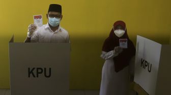 Calon Wakil Wali Kota Depok Imam Budi Hartono didampingi istrinya Etty Maryati Salim menunjukkan surat suara sebelum menggunakan hak pilih dalam Pilkada Depok di TPS 47, Kompleks Acacia, Grand Depok City, Depok, Jawa Barat, Rabu (9/12/2020). [Suara.com/Angga Budhiyanto]